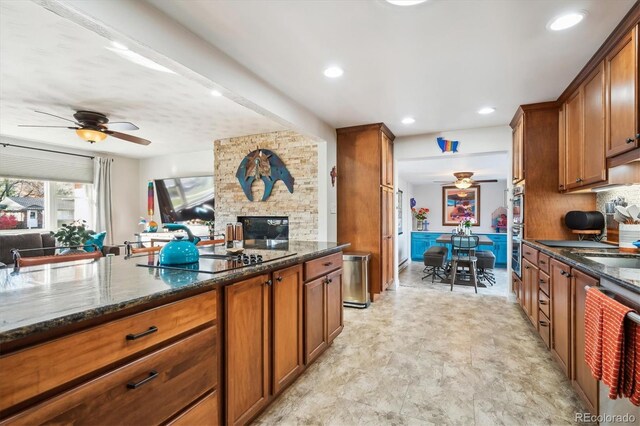 kitchen with a stone fireplace, ceiling fan, dark stone countertops, and stainless steel appliances