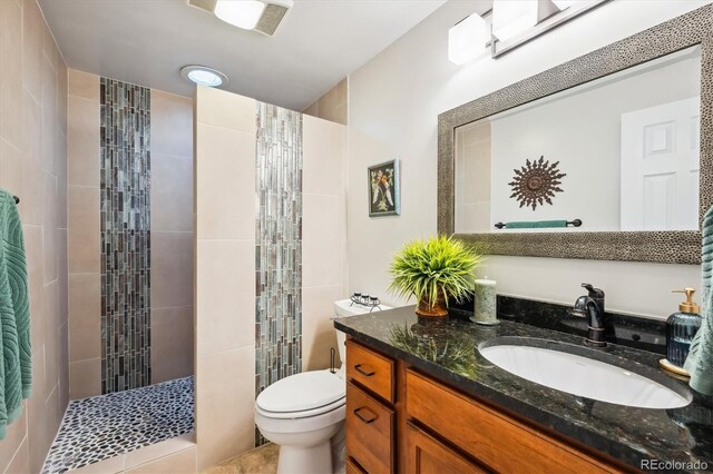 bathroom with tile patterned floors, vanity, toilet, and tiled shower