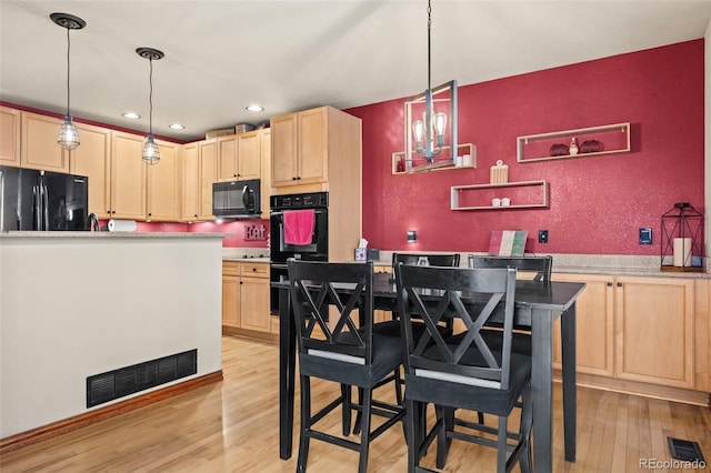 kitchen featuring light brown cabinets, decorative light fixtures, light hardwood / wood-style flooring, and black appliances