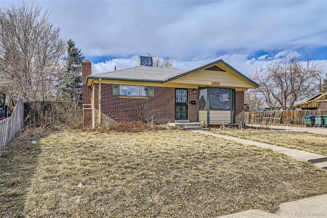 view of front of home with a front yard, brick siding, fence, and a chimney