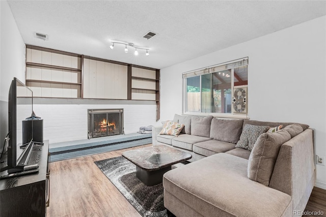 living room featuring hardwood / wood-style flooring, a textured ceiling, and a brick fireplace