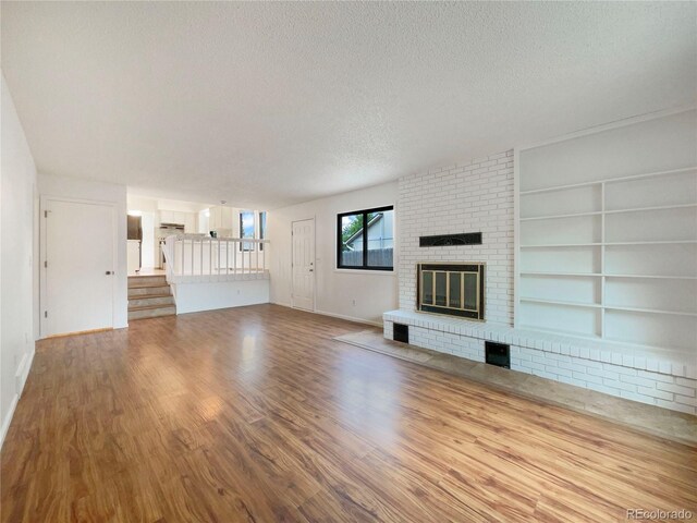 1460 Belmont Dr, Longmont, CO 80503 - unfurnished living room featuring a textured ceiling, a fireplace, wood finished floors, built in shelves, and stairs