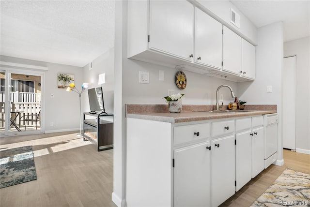 kitchen with sink, light hardwood / wood-style flooring, dishwasher, and white cabinets