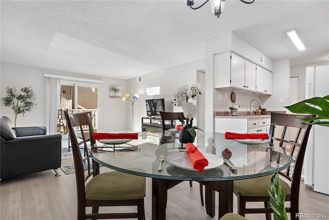 dining space featuring sink, light hardwood / wood-style floors, and a textured ceiling