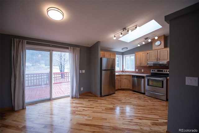 kitchen featuring lofted ceiling with skylight, light wood-style flooring, appliances with stainless steel finishes, under cabinet range hood, and a sink