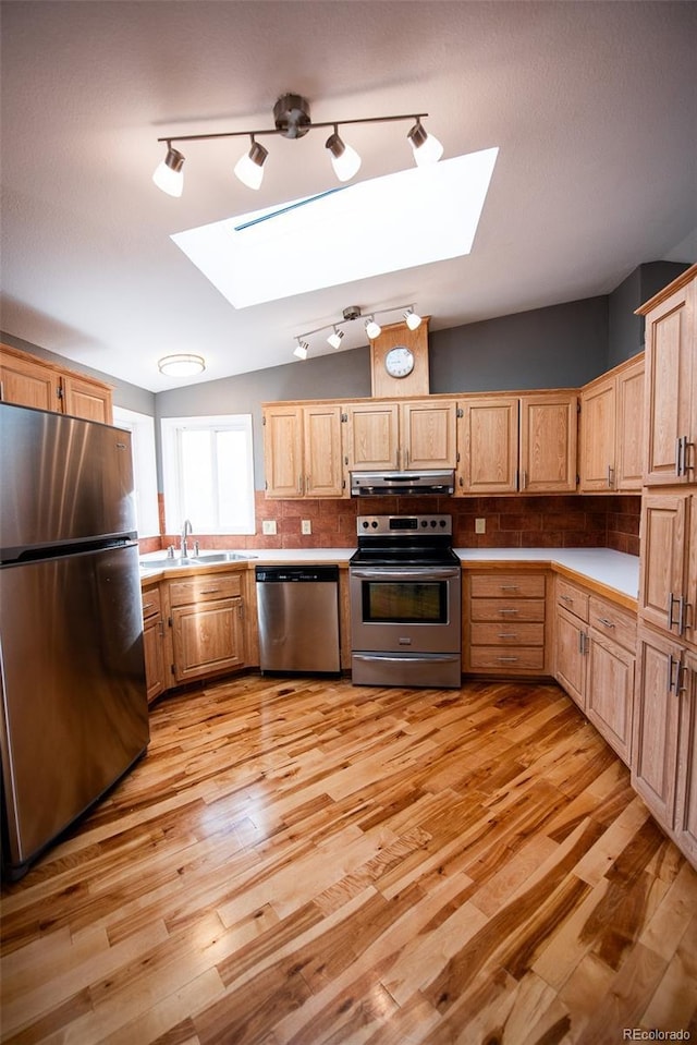 kitchen featuring vaulted ceiling with skylight, decorative backsplash, stainless steel appliances, light countertops, and under cabinet range hood