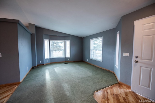 interior space with baseboards, vaulted ceiling, and light colored carpet