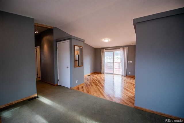 carpeted spare room with vaulted ceiling, wood finished floors, visible vents, and baseboards