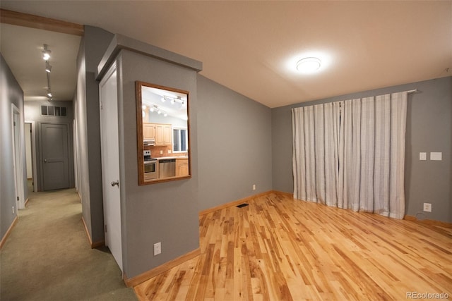 spare room with rail lighting, visible vents, vaulted ceiling, and wood finished floors