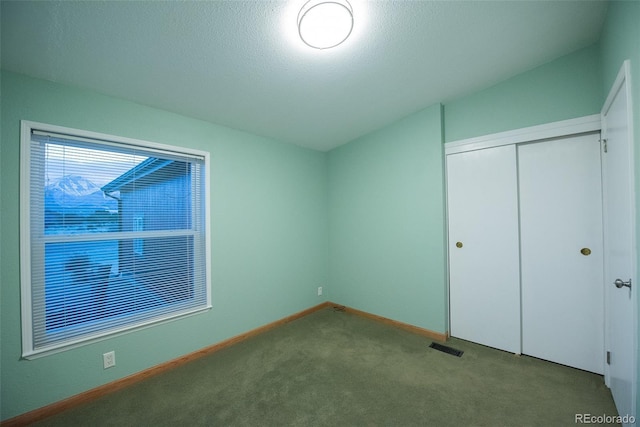 unfurnished bedroom with a textured ceiling, carpet flooring, visible vents, baseboards, and a closet