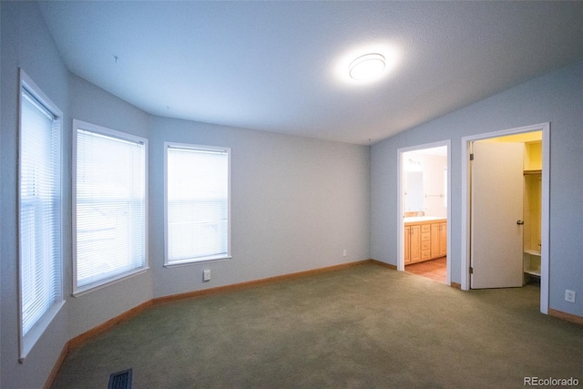 unfurnished bedroom with lofted ceiling, light colored carpet, visible vents, ensuite bath, and baseboards