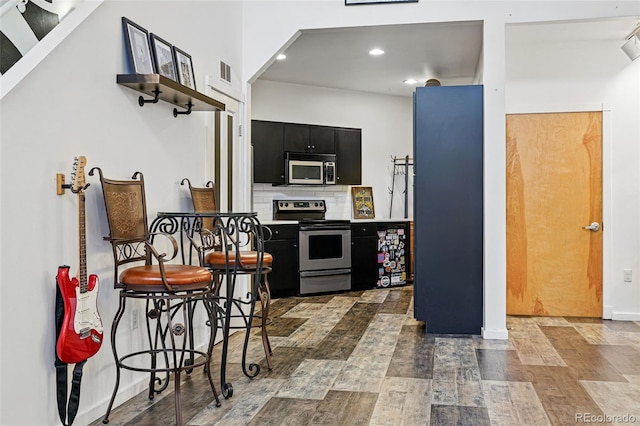kitchen with stainless steel appliances, dark cabinetry, wood finished floors, decorative backsplash, and recessed lighting