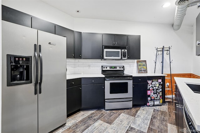 kitchen with appliances with stainless steel finishes, wood finished floors, light countertops, tasteful backsplash, and dark cabinets