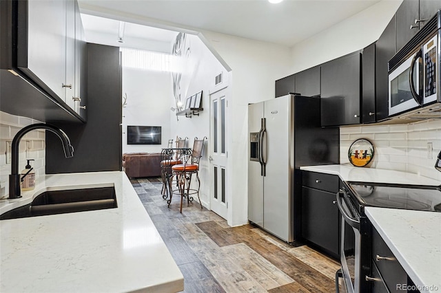 kitchen featuring dark cabinets, stainless steel appliances, a sink, and light wood-style flooring
