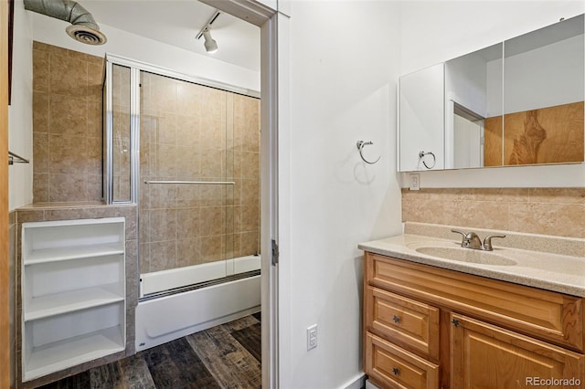 full bathroom with combined bath / shower with glass door, track lighting, vanity, wood finished floors, and backsplash