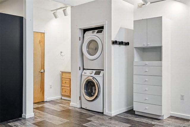 washroom featuring estacked washer and dryer, dark wood-style flooring, baseboards, and track lighting