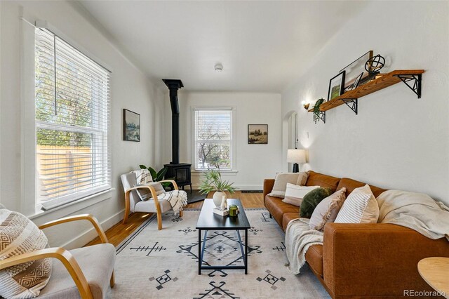 living area featuring arched walkways, baseboards, a wood stove, and light wood finished floors