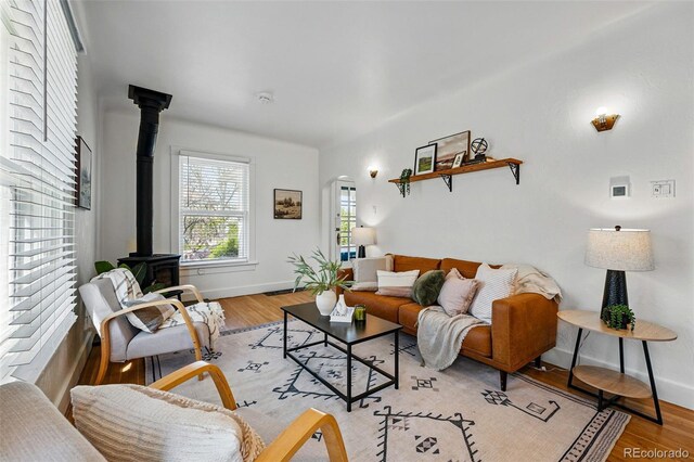 living room with baseboards, a wood stove, light wood finished floors, and arched walkways