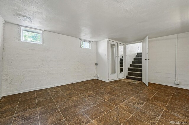 below grade area with stairs, a textured ceiling, baseboards, and a wealth of natural light