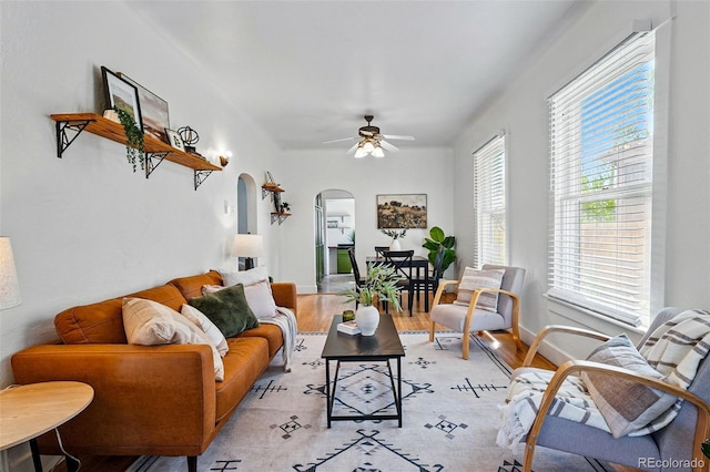 living room with arched walkways, a ceiling fan, and light wood-type flooring
