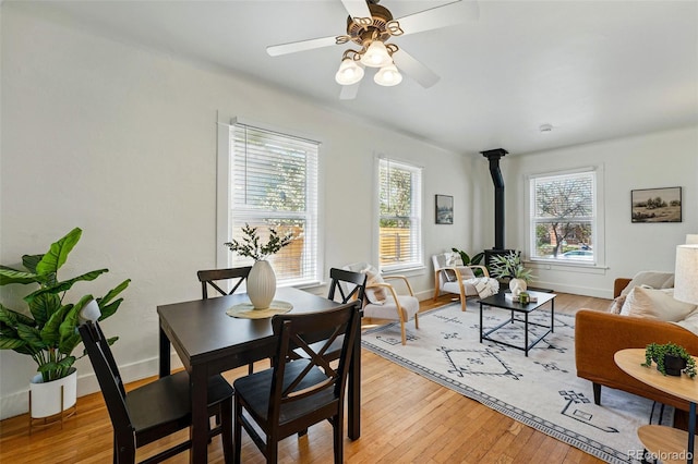 dining room with baseboards, ceiling fan, a wood stove, and light wood-type flooring