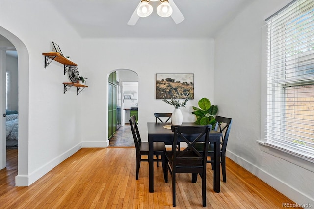 dining room featuring arched walkways, baseboards, a ceiling fan, and light wood-style flooring