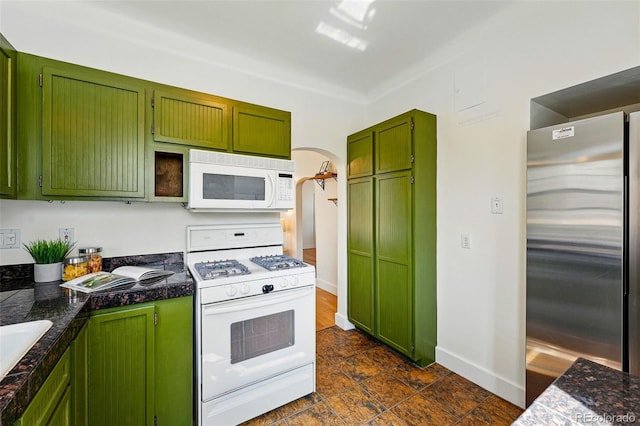 kitchen featuring green cabinetry, a sink, white appliances, arched walkways, and baseboards