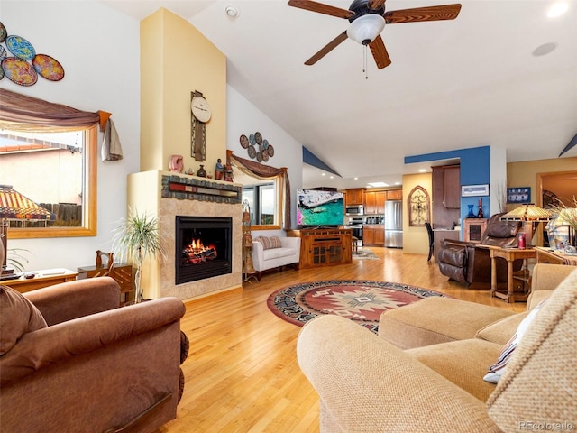 living room with high vaulted ceiling, light hardwood / wood-style floors, a tile fireplace, and ceiling fan