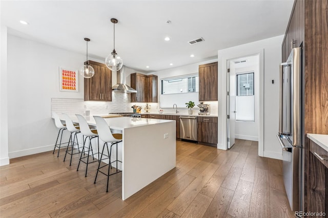 kitchen featuring wall chimney exhaust hood, a kitchen bar, hanging light fixtures, kitchen peninsula, and stainless steel appliances