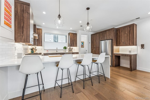 kitchen featuring high end fridge, a breakfast bar area, light wood-type flooring, pendant lighting, and backsplash