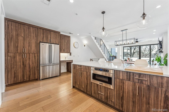 kitchen featuring dark brown cabinetry, high end fridge, decorative light fixtures, light wood-type flooring, and oven