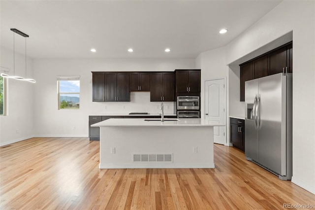 2423 Delicato Ct, Colorado Springs, CO 80921 - kitchen with stainless steel appliances, a sink, light countertops, light wood finished floors, and an island with sink