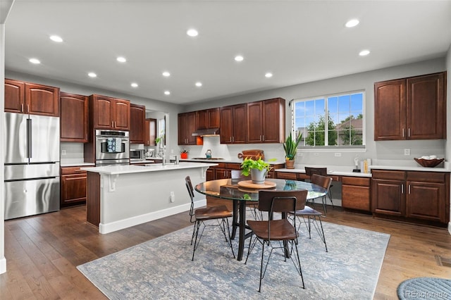 5984 S Paris Pl, Greenwood Village, CO 80111 - kitchen featuring appliances with stainless steel finishes, under cabinet range hood, a kitchen island with sink, light countertops, and recessed lighting