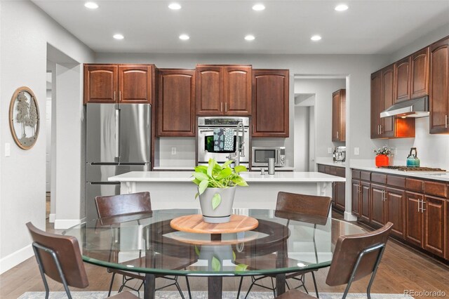 5984 S Paris Pl, Greenwood Village, CO 80111 - kitchen with appliances with stainless steel finishes, under cabinet range hood, recessed lighting, an island with sink, and light countertops