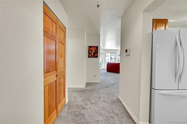 hallway featuring light colored carpet and a textured ceiling