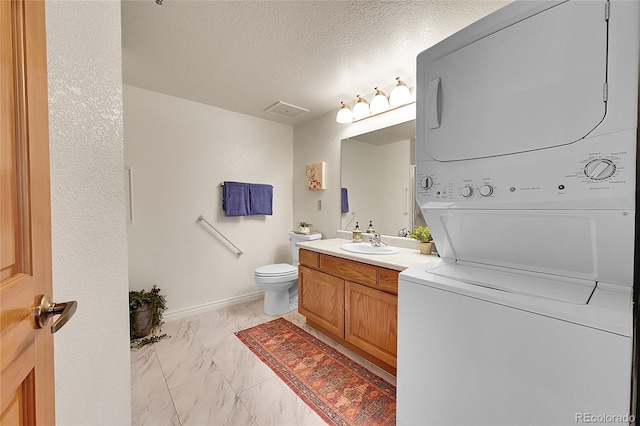 bathroom with a textured ceiling, toilet, stacked washer / dryer, and vanity