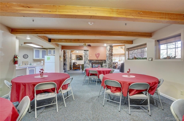 carpeted dining area featuring a stone fireplace and beamed ceiling