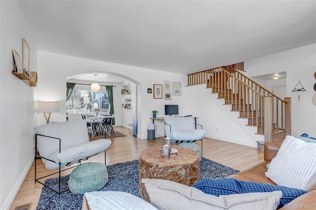 living room featuring stairway, arched walkways, baseboards, and wood finished floors