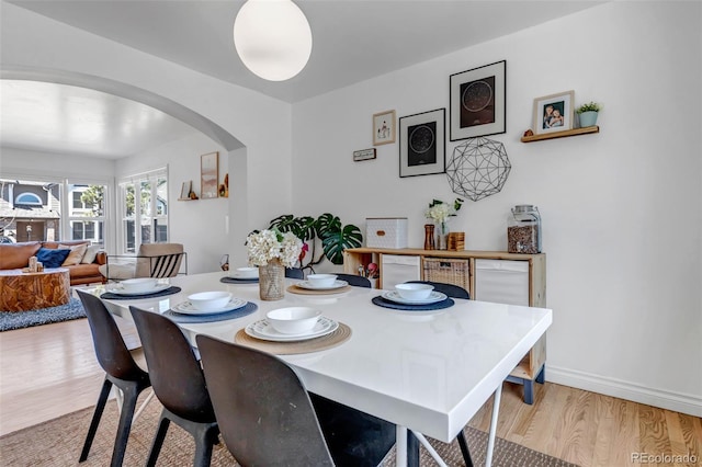 dining area with baseboards, arched walkways, and light wood-style floors