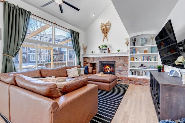 living area with built in shelves, a ceiling fan, wood finished floors, high vaulted ceiling, and a brick fireplace