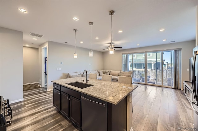 kitchen featuring dishwashing machine, light stone counters, open floor plan, wood finished floors, and a sink