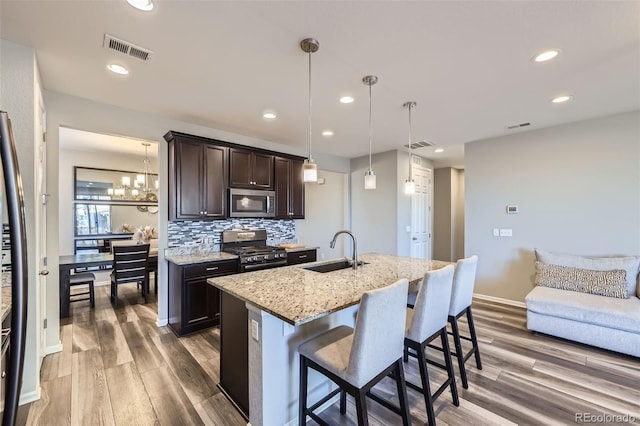 kitchen with dark brown cabinetry, visible vents, appliances with stainless steel finishes, a sink, and backsplash