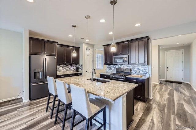 kitchen with appliances with stainless steel finishes, a sink, dark brown cabinetry, and light stone countertops