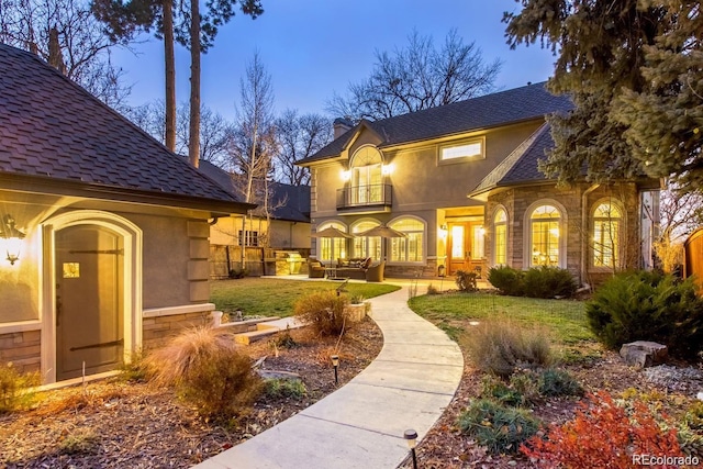1160 Monaco Pkwy, Denver, CO 80220 - view of front of house featuring a balcony, a patio area, a front lawn, stucco siding, and a shingled roof