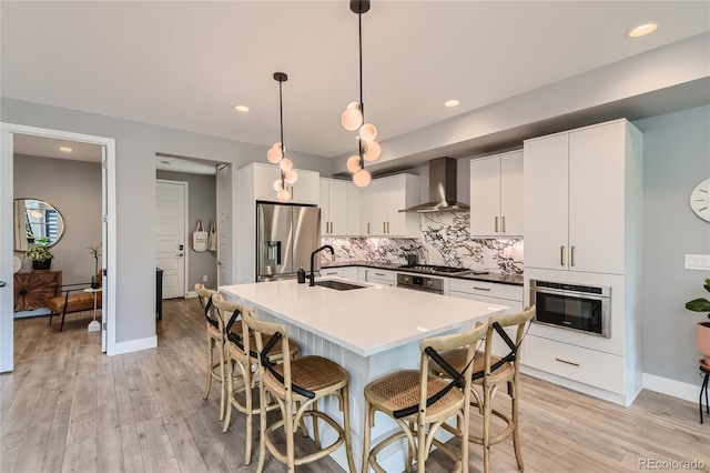 kitchen featuring a sink, appliances with stainless steel finishes, decorative backsplash, wall chimney exhaust hood, and a kitchen bar