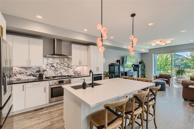 kitchen featuring wall chimney exhaust hood, open floor plan, a sink, stainless steel appliances, and backsplash