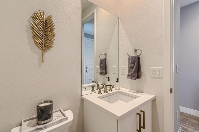 half bathroom featuring toilet, a textured wall, wood finished floors, and vanity