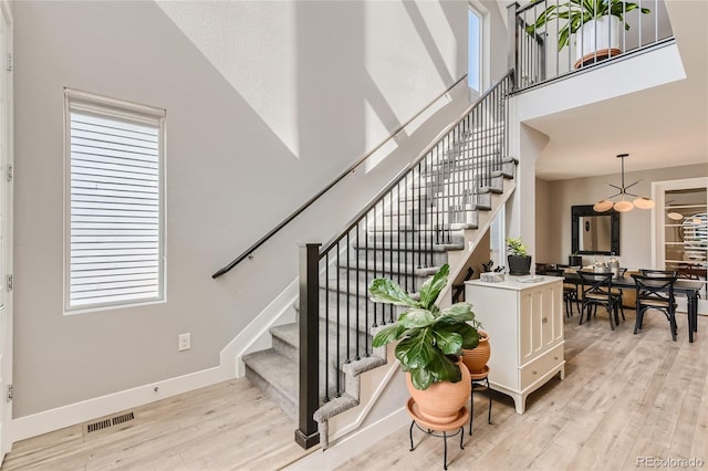 staircase with visible vents, wood finished floors, a towering ceiling, and baseboards