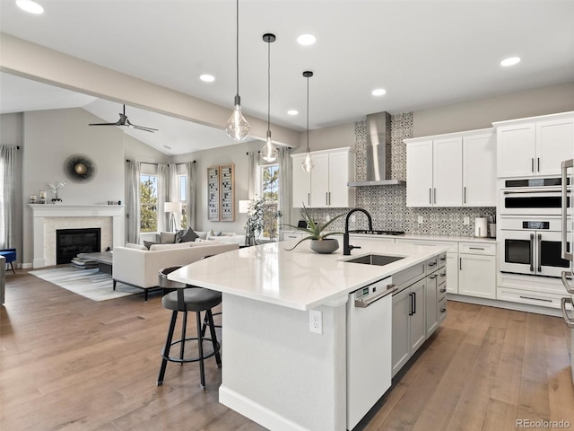 kitchen featuring a sink, a glass covered fireplace, white appliances, light wood-style floors, and wall chimney exhaust hood