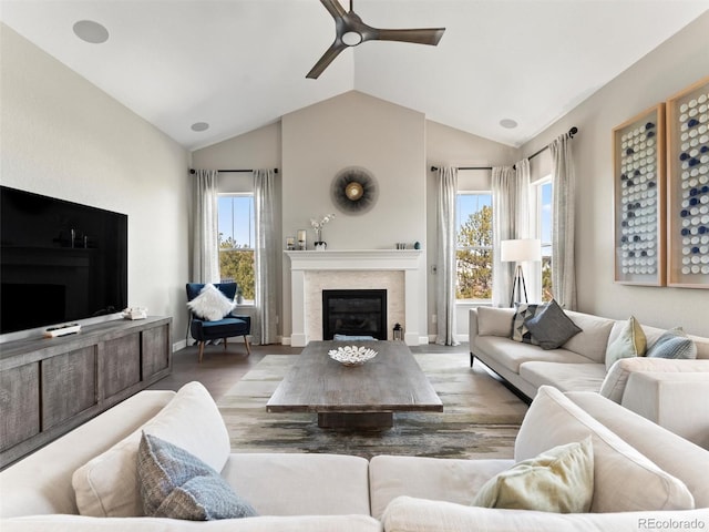 living room with a wealth of natural light, a glass covered fireplace, a ceiling fan, and vaulted ceiling